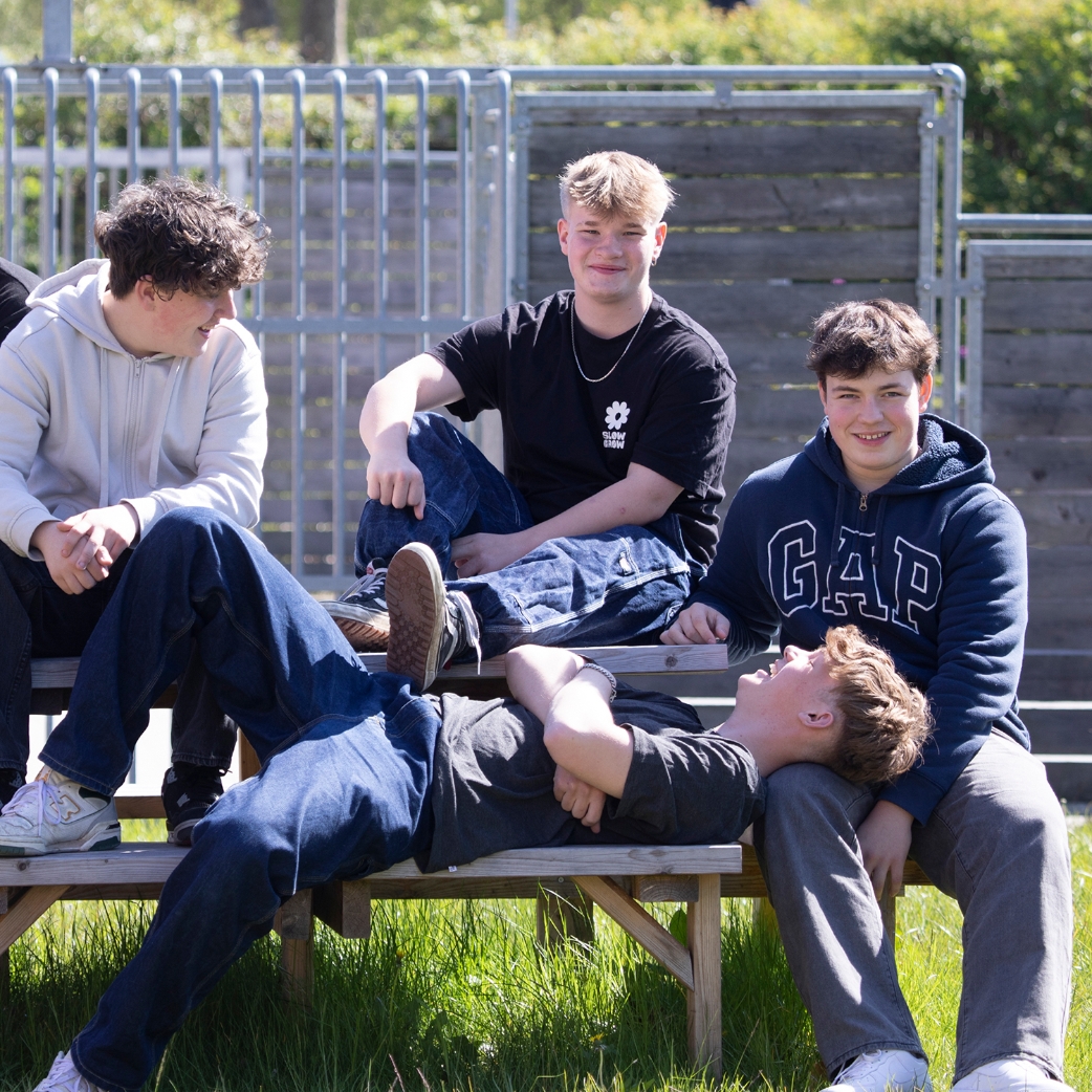 En gruppe elever fra NEG sidder på et bord bænkesæt udenfor. Drengene ser afslappet og glade ud.